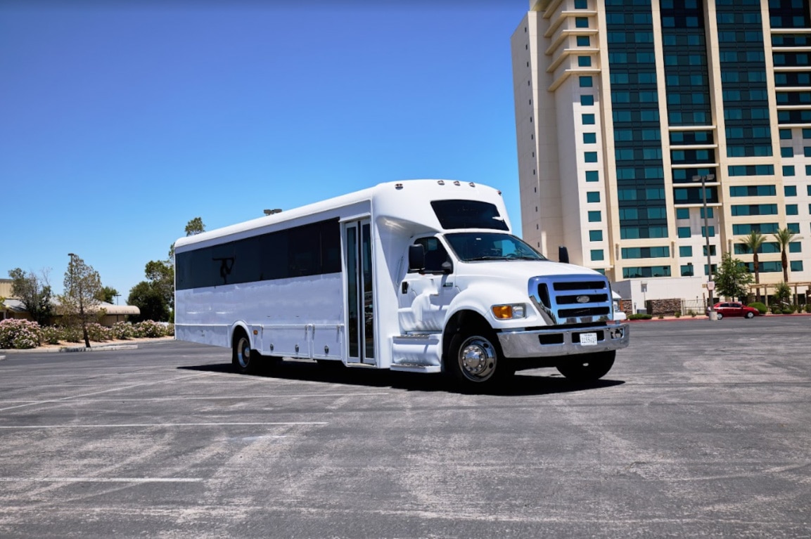 Bankroll 38-passenger white Las Vegas party bus parked in front of a hotel on a sunny day — great for group events.